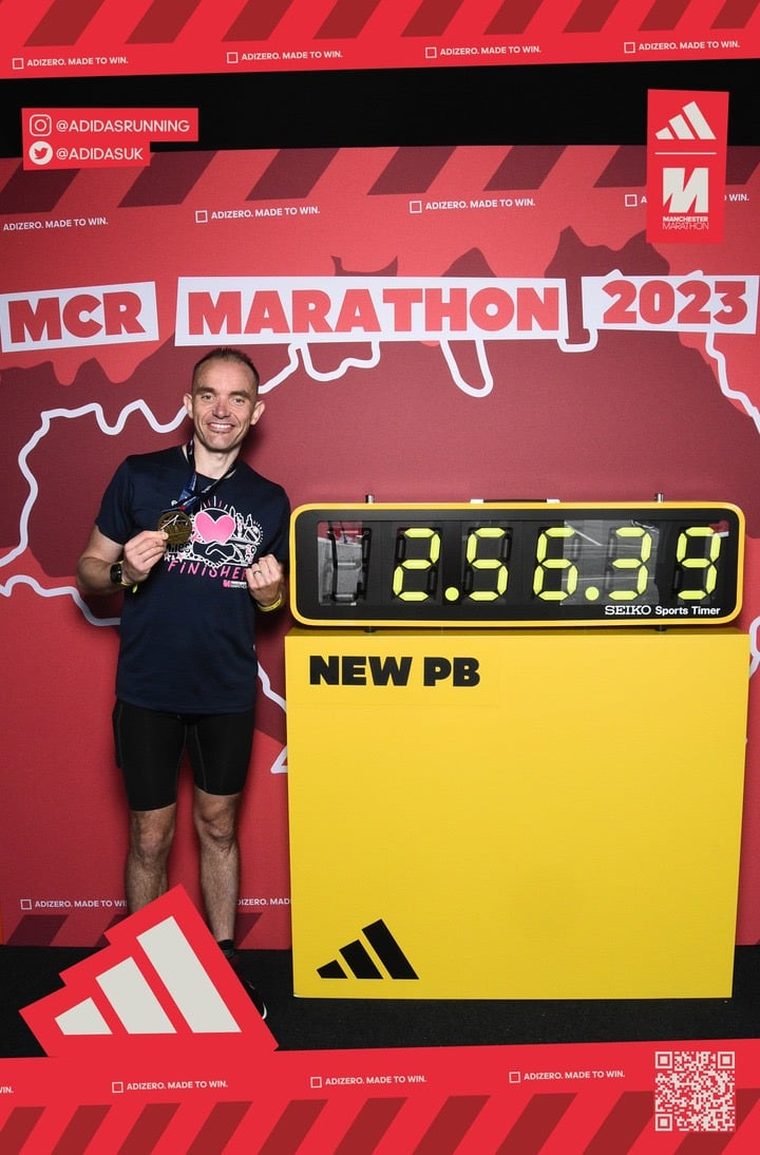 John at the Manchester Marathon 2023 finish board showing a new personal best of 2:58:39